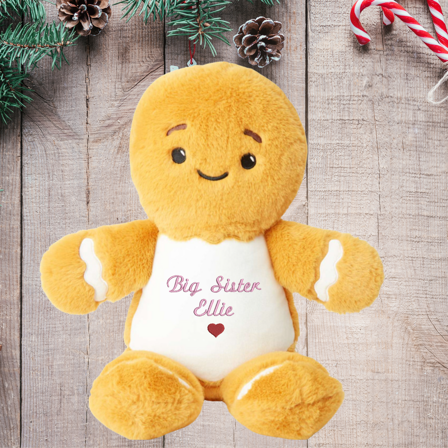 Plush gingerbread bear with 'Big Sister Ellie' text on a wooden surface with Christmas decorations.