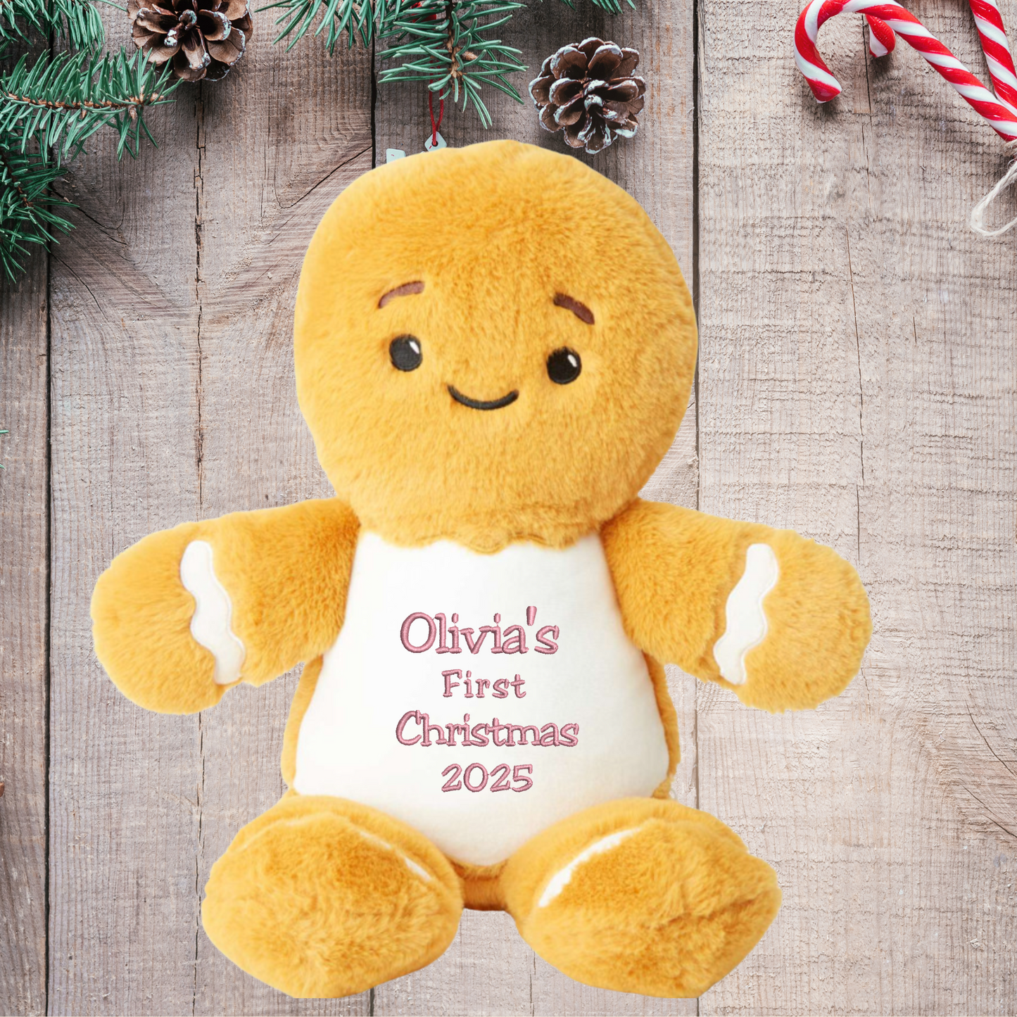 Plush gingerbread man toy with 'Olivia's First Christmas 2025' text on a wooden background with Christmas decorations.